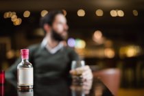 Close-up of small liquor bottle on table in bar with man in background — Stock Photo
