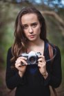 Portrait of beautiful woman standing with camera in forest — Stock Photo