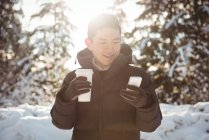 Улыбающийся мужчина в теплой одежде с помощью мобильного телефона зимой — стоковое фото