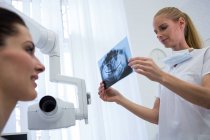 Dentiste regardant plaque de radiographie dentaire en face du patient à la clinique — Photo de stock