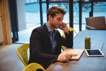 Empresário falando no telefone celular enquanto faz lanche no café — Fotografia de Stock