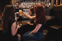 Amici felici brindare con bicchieri di birra al bancone del bar — Foto stock