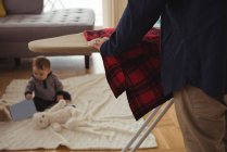 Vater bügelt Hemd, während Baby zu Hause im Hintergrund spielt — Stockfoto