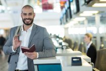 Portrait of smiling businessman standing at check-in counter with passport and boarding pass at airport terminal — Stock Photo
