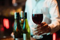Partie médiane du barman tenant un verre de vin rouge au comptoir du bar — Photo de stock
