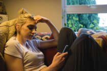 Жінка лежить і використовує мобільний телефон на дивані у вітальні — стокове фото
