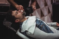 Средняя часть парикмахера наносит крем на бороду клиента в парикмахерской — стоковое фото