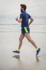 Schöner Athlet läuft am Sandstrand — Stockfoto
