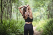 Vista posteriore della donna che esegue esercizio di stretching nella foresta — Foto stock