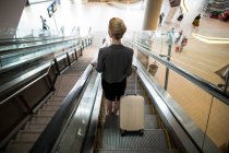 Вид сзади на деловую женщину, стоящую на эскалаторе с багажом в аэропорту — стоковое фото