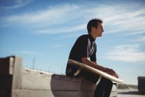 Surfista atencioso sentado em uma plataforma de madeira com prancha de surf na praia — Fotografia de Stock