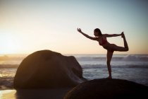 Femme effectuant des exercices d'étirement sur la plage au crépuscule — Photo de stock