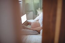 Mujer embarazada relajándose en la cama en el dormitorio - foto de stock
