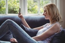Schöne Frau sitzt auf Sofa und benutzt Handy im Wohnzimmer zu Hause — Stockfoto