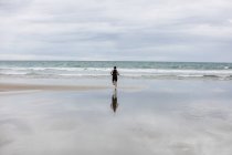 Vista trasera del hombre en traje de baño y gorra de natación corriendo en la playa - foto de stock