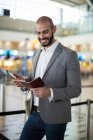 Empresário sorridente segurando um cartão de embarque e verificando seu telefone celular no terminal do aeroporto — Fotografia de Stock
