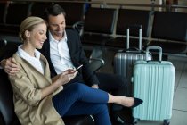 Casal feliz usando telefone celular no aeroporto — Fotografia de Stock