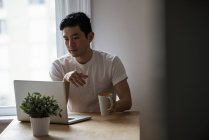 Человек смотрит на ноутбук во время чашки кофе дома — стоковое фото