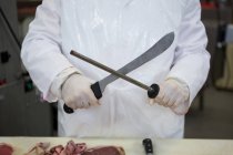 Мясник точит нож на мясокомбинате — стоковое фото