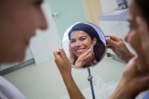 Щаслива жінка перевіряє шкіру у дзеркалі після отримання косметичного лікування — стокове фото
