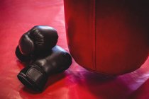 Luvas de boxe e saco de perfuração na superfície vermelha no estúdio de fitness — Fotografia de Stock