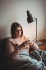 Женщина сидит на диване, используя мобильный телефон дома — стоковое фото