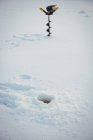 Close-up of ice fishing drill near hole in snow — Stock Photo