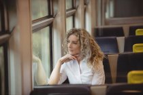 Pensativa mujer de negocios mirando hacia otro lado en tren mientras viaja - foto de stock