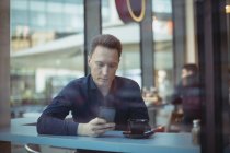 Мужчина, использующий мобильный телефон у стойки в столовой — стоковое фото