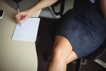 Vista ritagliata della donna d'affari che scrive sul blocco note in ufficio — Foto stock
