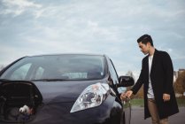 Homme ouvrant la porte de la voiture électrique à la station de recharge du véhicule électrique — Photo de stock