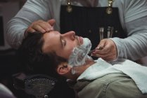Client getting beard shaved with razor in barber shop — Stock Photo