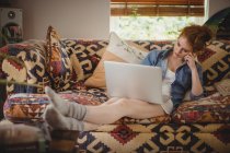 Donna premurosa che utilizza il computer portatile sul divano a casa — Foto stock