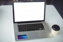 Primo piano del computer portatile con tazza di caffè usa e getta e carta di credito sul tavolo in caf ?? — Foto stock