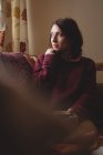 Mujer pensativa sentada y sosteniendo una taza de café en casa - foto de stock