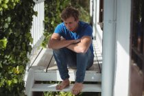 Uomo preoccupato seduto con le braccia incrociate sul portico — Foto stock