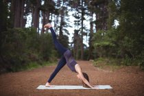 Жінка виконує йогу на тренувальному килимку в лісі — стокове фото