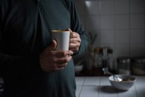 Середина человека, держащего чашку кофе дома — стоковое фото