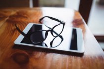 Tablet digital com óculos na mesa no café — Fotografia de Stock