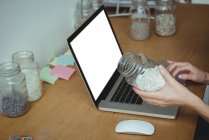Business executive using laptop while holding jar of pebbles in office — Stock Photo