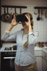 Mulher experimentando fone de ouvido realidade virtual na cozinha em casa — Fotografia de Stock
