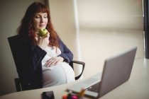 Pregnant businesswoman having apple in office — Stock Photo