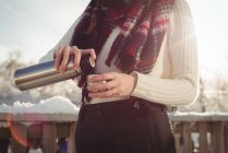 Середина жінки в зимовому одязі наливає напій у чашку під час лижних канікул — стокове фото