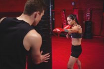 Female boxer practicing with trainer at fitness studio — Stock Photo
