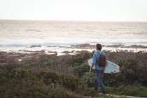 Homme portant une planche de surf marchant vers la mer — Photo de stock