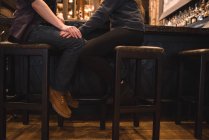 Sección baja de pareja romántica sentada en taburetes en el mostrador del bar - foto de stock