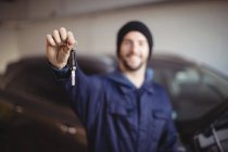 Smiling mechanic in garage holding car key — Stock Photo