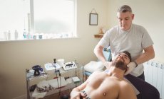 Физиотерапевт осматривает шею пациента-мужчины в клинике — стоковое фото