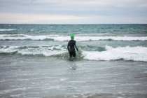 Vista traseira do atleta em terno molhado caminhando em direção ao mar — Fotografia de Stock
