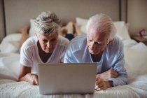 Coppia anziana sdraiata sul letto e utilizzando il computer portatile in camera da letto — Foto stock